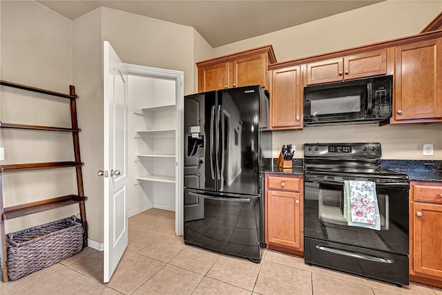 kitchen with baseboards, brown cabinetry, light tile patterned floors, and black appliances