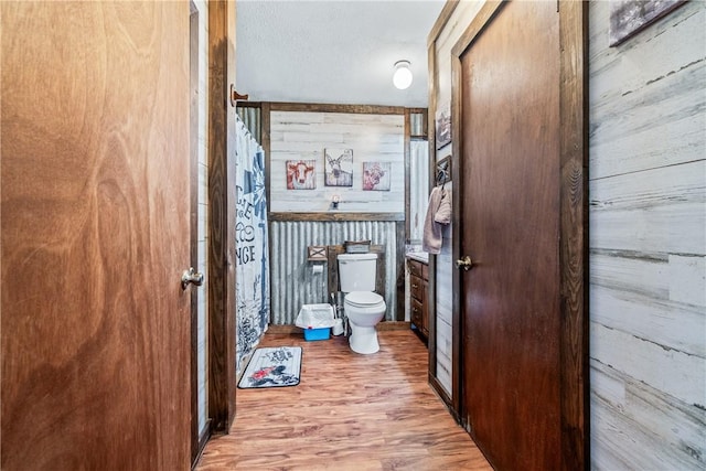 bathroom featuring wooden walls, toilet, and wood finished floors