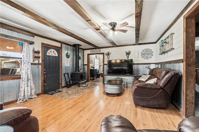 living area featuring beamed ceiling, wood finished floors, wood walls, ceiling fan, and a wood stove