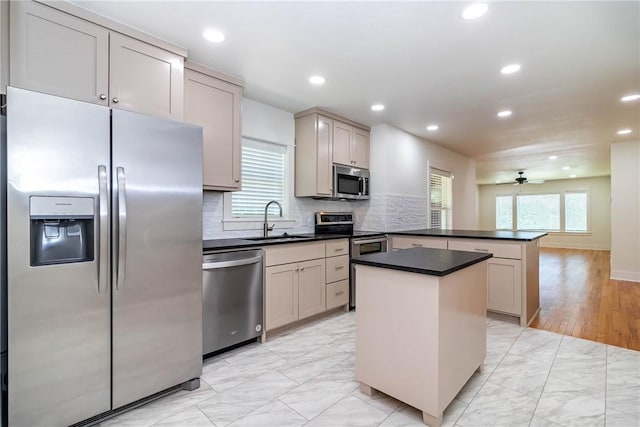 kitchen featuring dark countertops, appliances with stainless steel finishes, a peninsula, a sink, and backsplash