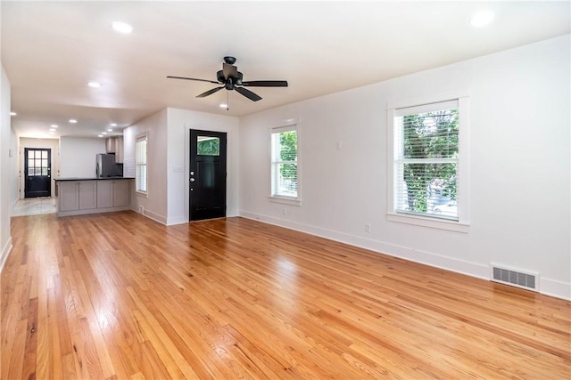 unfurnished living room featuring light wood-style floors, a wealth of natural light, visible vents, and baseboards