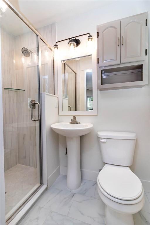 full bathroom with marble finish floor, a shower stall, toilet, and baseboards