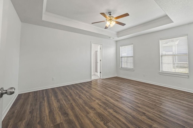 unfurnished room with dark wood-type flooring, a tray ceiling, crown molding, and baseboards