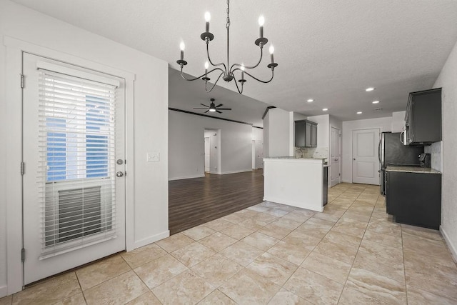 kitchen with light tile patterned floors, a textured ceiling, ceiling fan with notable chandelier, light countertops, and decorative backsplash