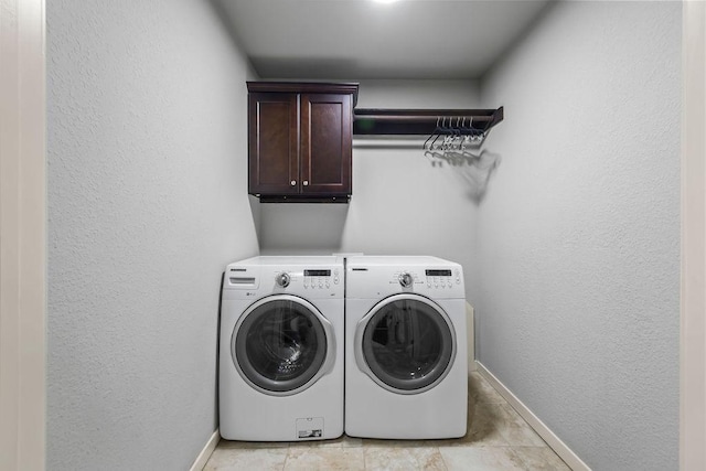 clothes washing area with a textured wall, washing machine and clothes dryer, cabinet space, and baseboards