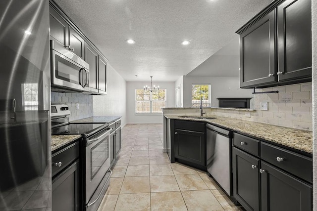 kitchen featuring light stone counters, stainless steel appliances, light tile patterned flooring, a sink, and a peninsula