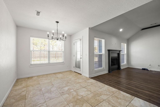 unfurnished dining area featuring tile patterned flooring, vaulted ceiling, a textured ceiling, a fireplace, and a chandelier