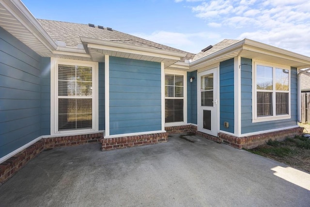 property entrance with roof with shingles and a patio