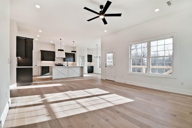 unfurnished living room with recessed lighting, ceiling fan with notable chandelier, visible vents, baseboards, and light wood-style floors