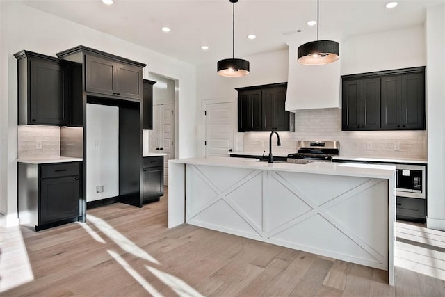 kitchen featuring light wood finished floors, an island with sink, light countertops, stainless steel range with gas cooktop, and a sink