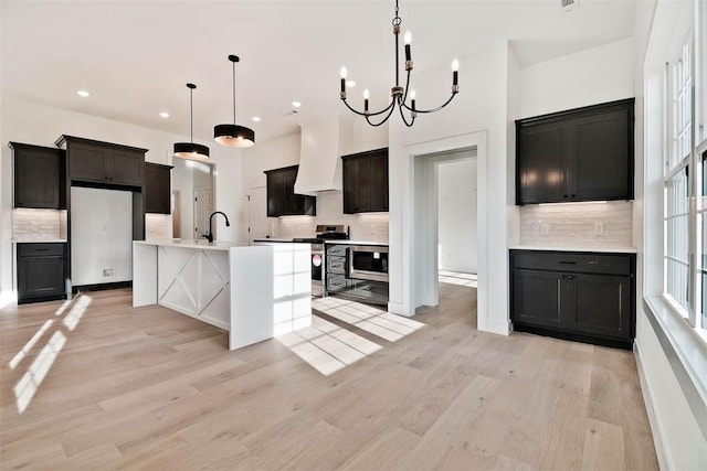 kitchen with premium range hood, a sink, appliances with stainless steel finishes, backsplash, and light wood finished floors