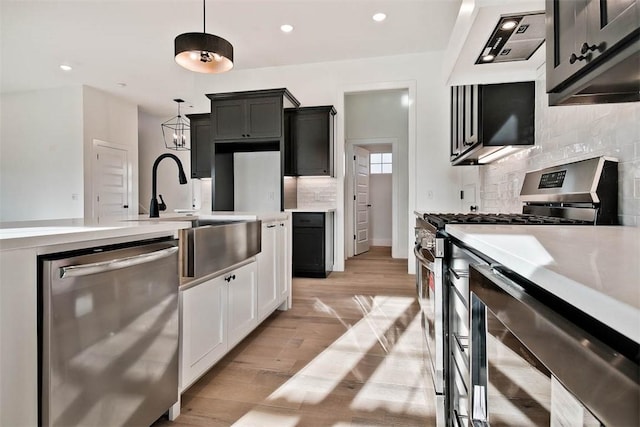 kitchen with light countertops, hanging light fixtures, appliances with stainless steel finishes, a sink, and light wood-type flooring