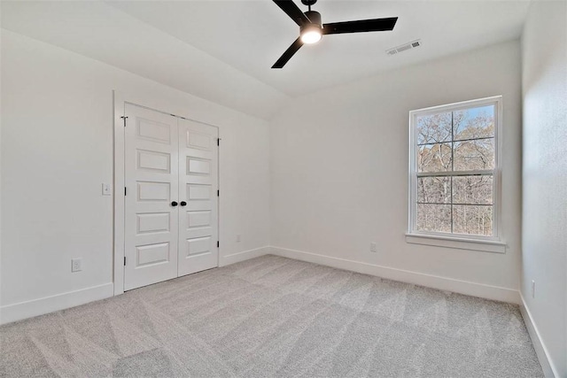 spare room with light colored carpet, visible vents, a ceiling fan, vaulted ceiling, and baseboards