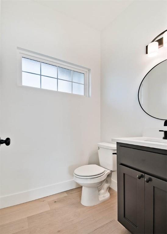 half bathroom featuring toilet, wood finished floors, vanity, and baseboards