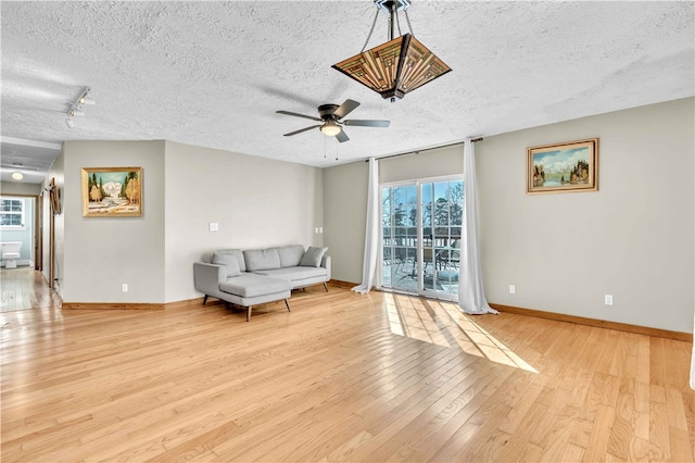 living area featuring light wood finished floors, a ceiling fan, baseboards, and a textured ceiling