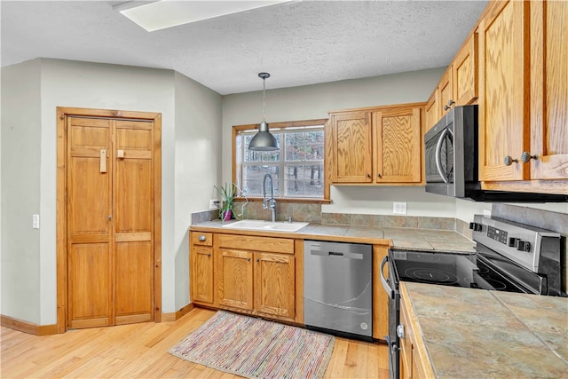 kitchen with pendant lighting, tile counters, light wood-style flooring, appliances with stainless steel finishes, and a sink