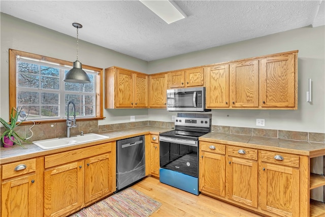 kitchen featuring light wood finished floors, appliances with stainless steel finishes, decorative light fixtures, a textured ceiling, and a sink