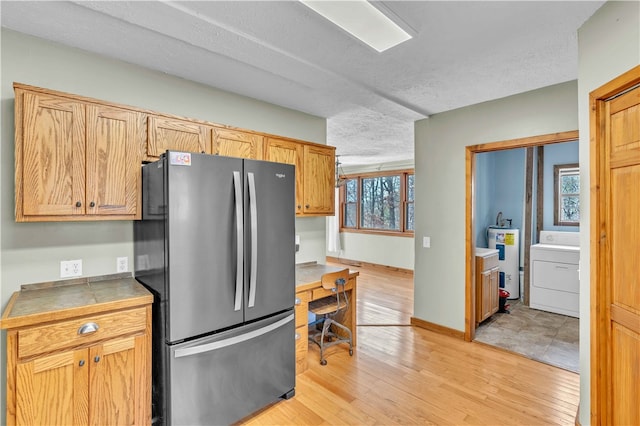 kitchen featuring washer / dryer, light wood finished floors, electric water heater, freestanding refrigerator, and a textured ceiling