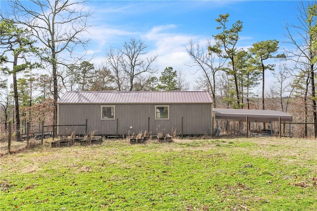 rear view of property featuring a carport, a lawn, an outdoor structure, and fence