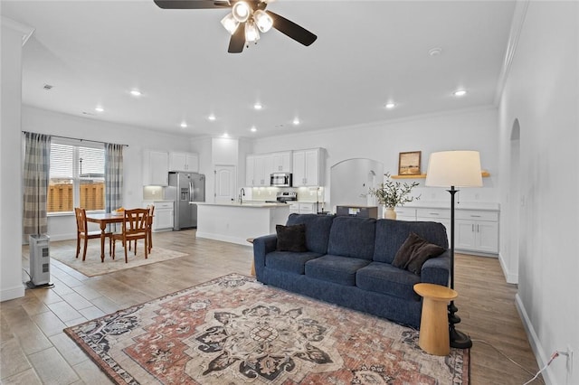 living area featuring light wood-style floors, arched walkways, crown molding, and baseboards