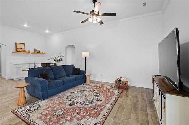 living room with light wood-style floors, arched walkways, visible vents, and crown molding