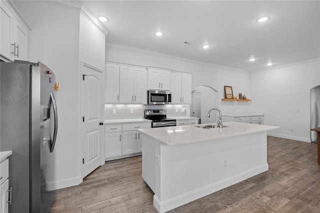 kitchen featuring arched walkways, light wood-style flooring, appliances with stainless steel finishes, ornamental molding, and a sink