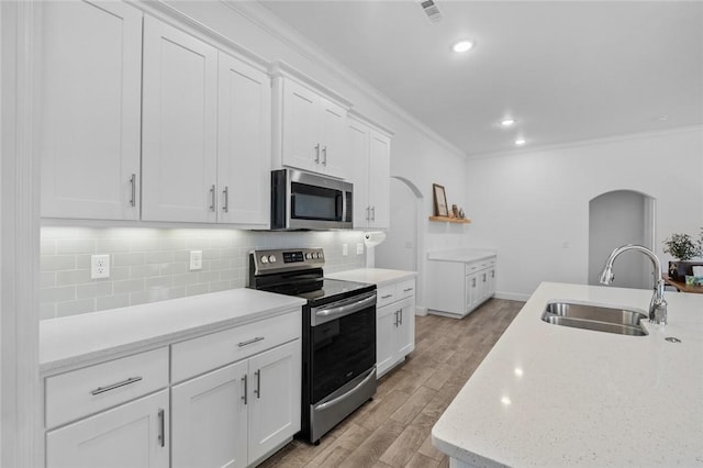 kitchen with arched walkways, stainless steel appliances, ornamental molding, and a sink