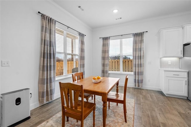 dining room with light wood finished floors, a healthy amount of sunlight, visible vents, and crown molding