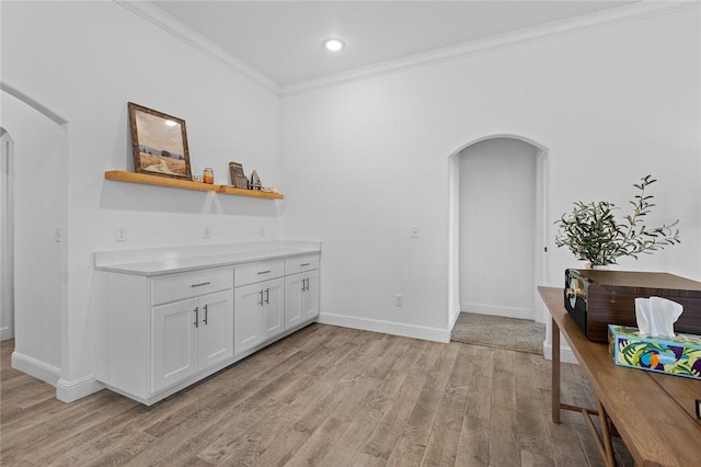 interior space with arched walkways, light countertops, ornamental molding, light wood-style floors, and white cabinetry