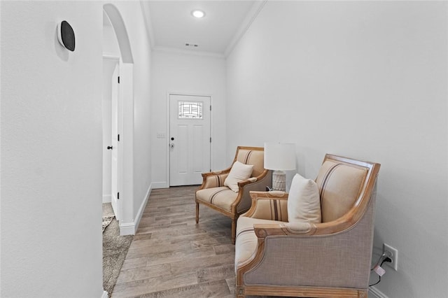 foyer entrance with baseboards, visible vents, arched walkways, ornamental molding, and light wood-style floors