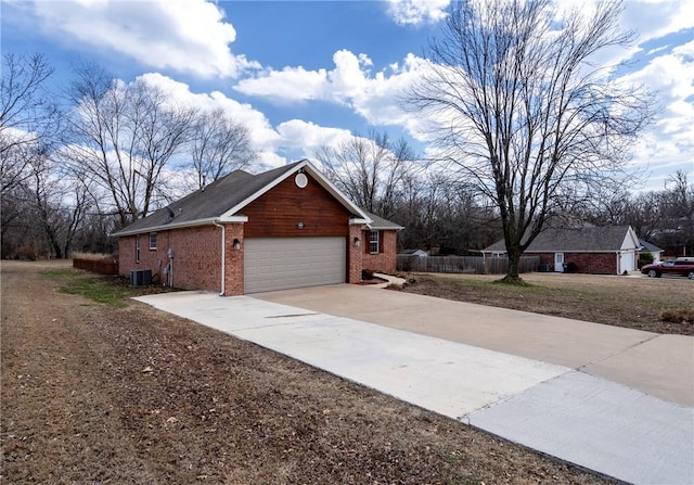 view of side of home featuring brick siding, central air condition unit, an attached garage, fence, and driveway