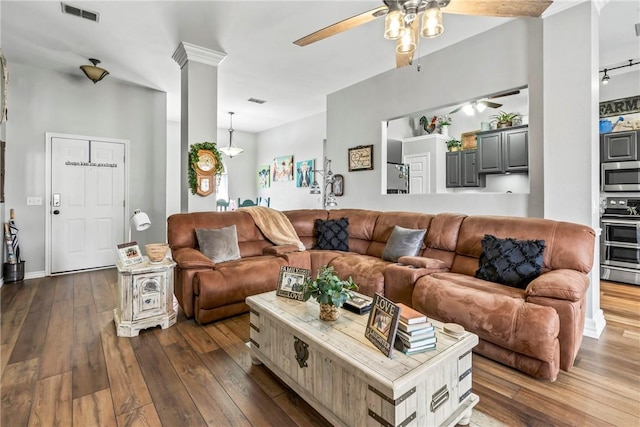 living area featuring dark wood-style floors, ceiling fan, visible vents, and ornate columns