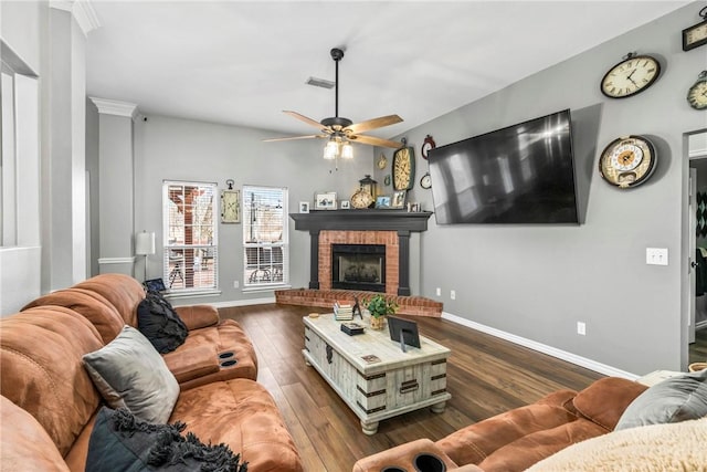 living room with dark wood-style flooring, visible vents, a ceiling fan, a brick fireplace, and baseboards