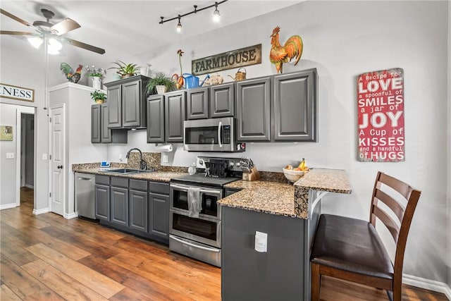 kitchen with a breakfast bar, gray cabinets, appliances with stainless steel finishes, dark wood-type flooring, and a sink