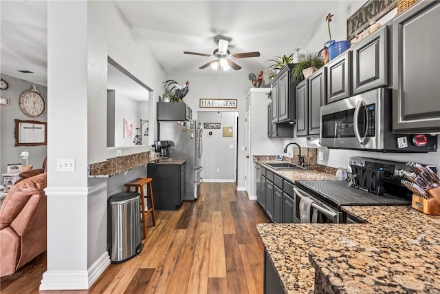 kitchen with dark wood finished floors, ceiling fan, stainless steel appliances, stone counters, and a sink