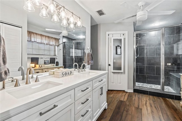 full bathroom with a stall shower, double vanity, a sink, and wood finished floors