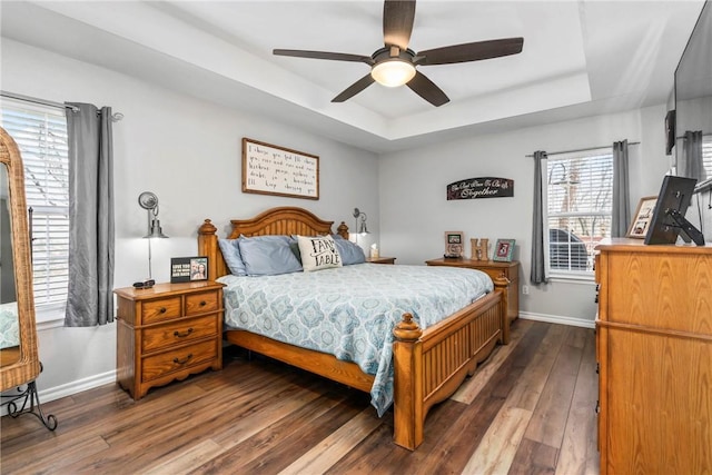 bedroom with dark wood-type flooring, a raised ceiling, baseboards, and a ceiling fan