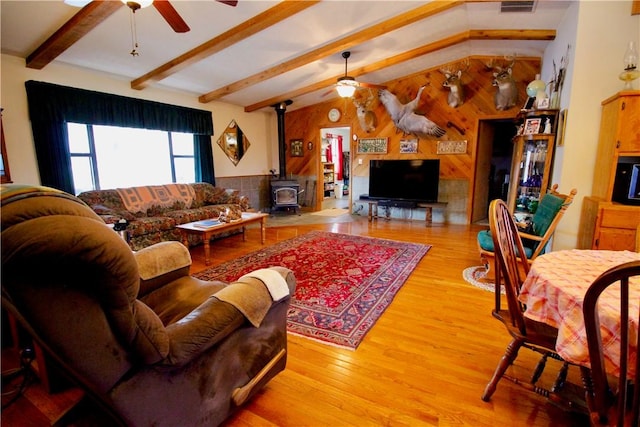 living area featuring a wood stove, ceiling fan, wooden walls, and wood finished floors