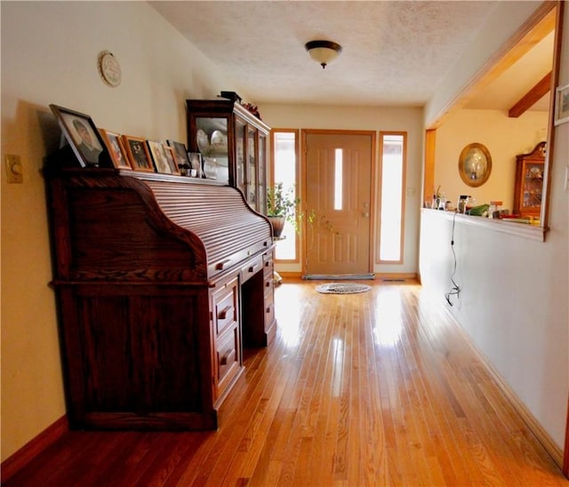 entrance foyer with hardwood / wood-style flooring, beam ceiling, baseboards, and a textured ceiling