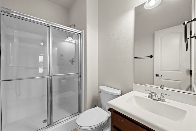 bathroom with a shower stall, toilet, vanity, and a textured wall