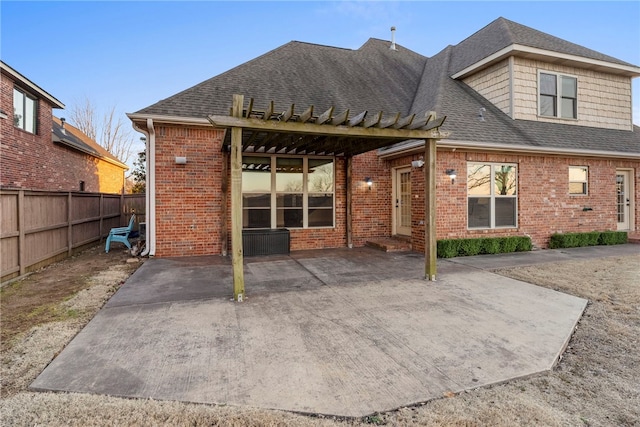 back of property featuring brick siding, fence, roof with shingles, a patio area, and a pergola