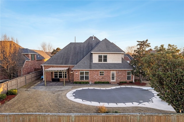 rear view of house featuring a patio, brick siding, roof with shingles, and a fenced backyard