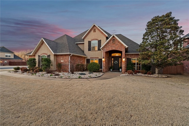 traditional-style house with brick siding, a shingled roof, fence, stucco siding, and a lawn