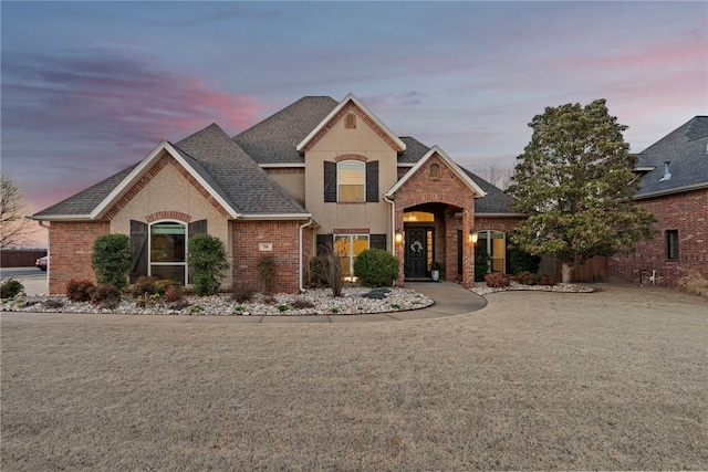 view of front of house featuring stucco siding, brick siding, a front lawn, and a shingled roof