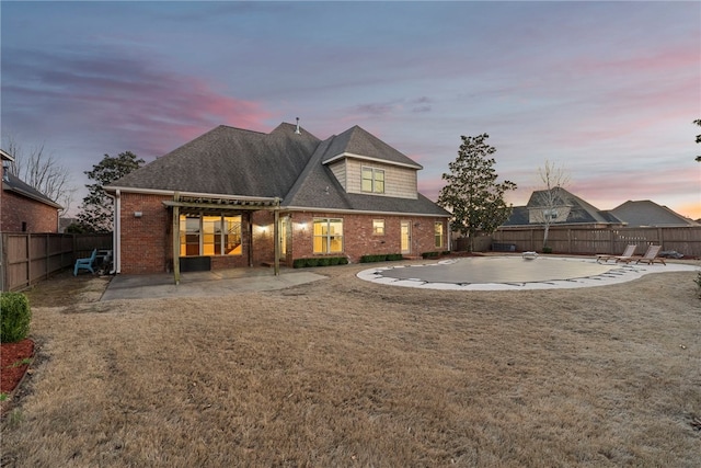 back of house at dusk with a yard, brick siding, a fenced backyard, and a patio area