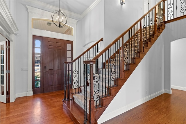 foyer entrance featuring baseboards, wood finished floors, a towering ceiling, and crown molding