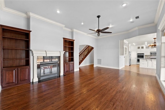 unfurnished living room featuring crown molding, ceiling fan, a fireplace with flush hearth, wood finished floors, and arched walkways