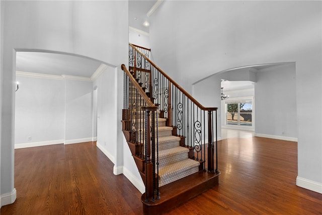 staircase with crown molding, wood finished floors, arched walkways, and baseboards