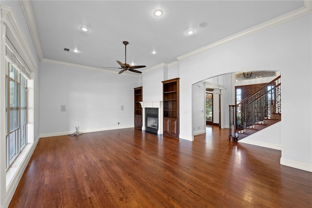 unfurnished living room with a ceiling fan, wood finished floors, a glass covered fireplace, arched walkways, and stairs