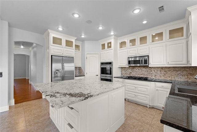 kitchen featuring visible vents, a kitchen island, arched walkways, appliances with stainless steel finishes, and decorative backsplash